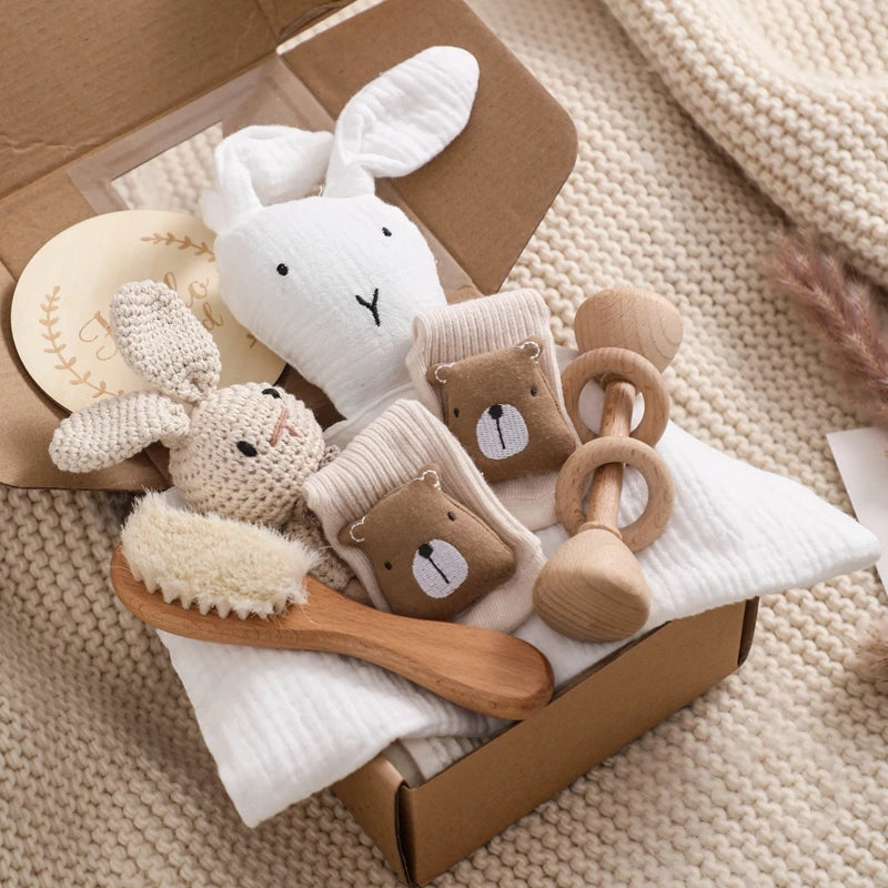 Collection of baby toys including a plush rabbit, wooden rattle, and soft toys in a box on a textured surface.